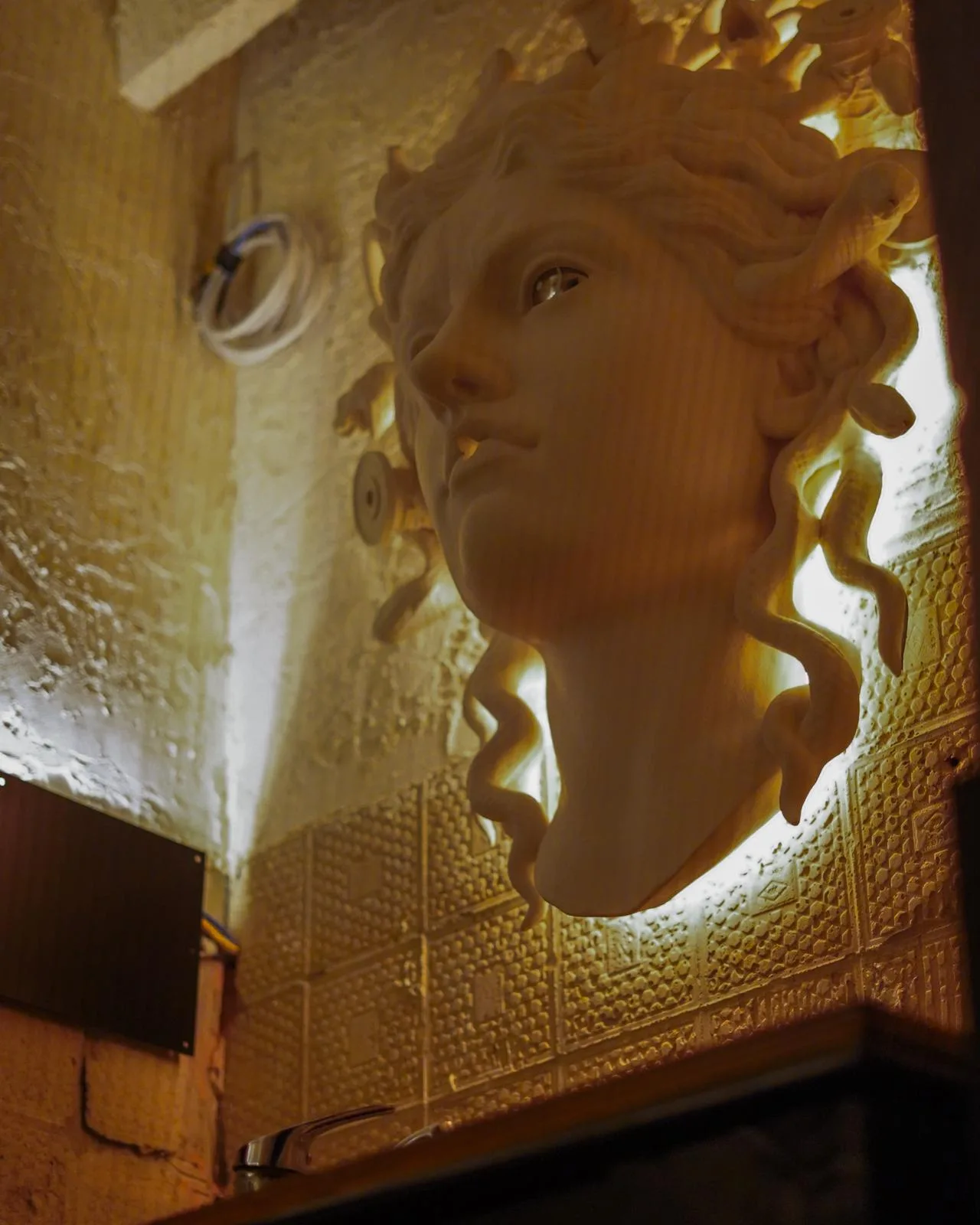 Detaliu sculptural iluminat pe un perete cu suprafață reliefată.